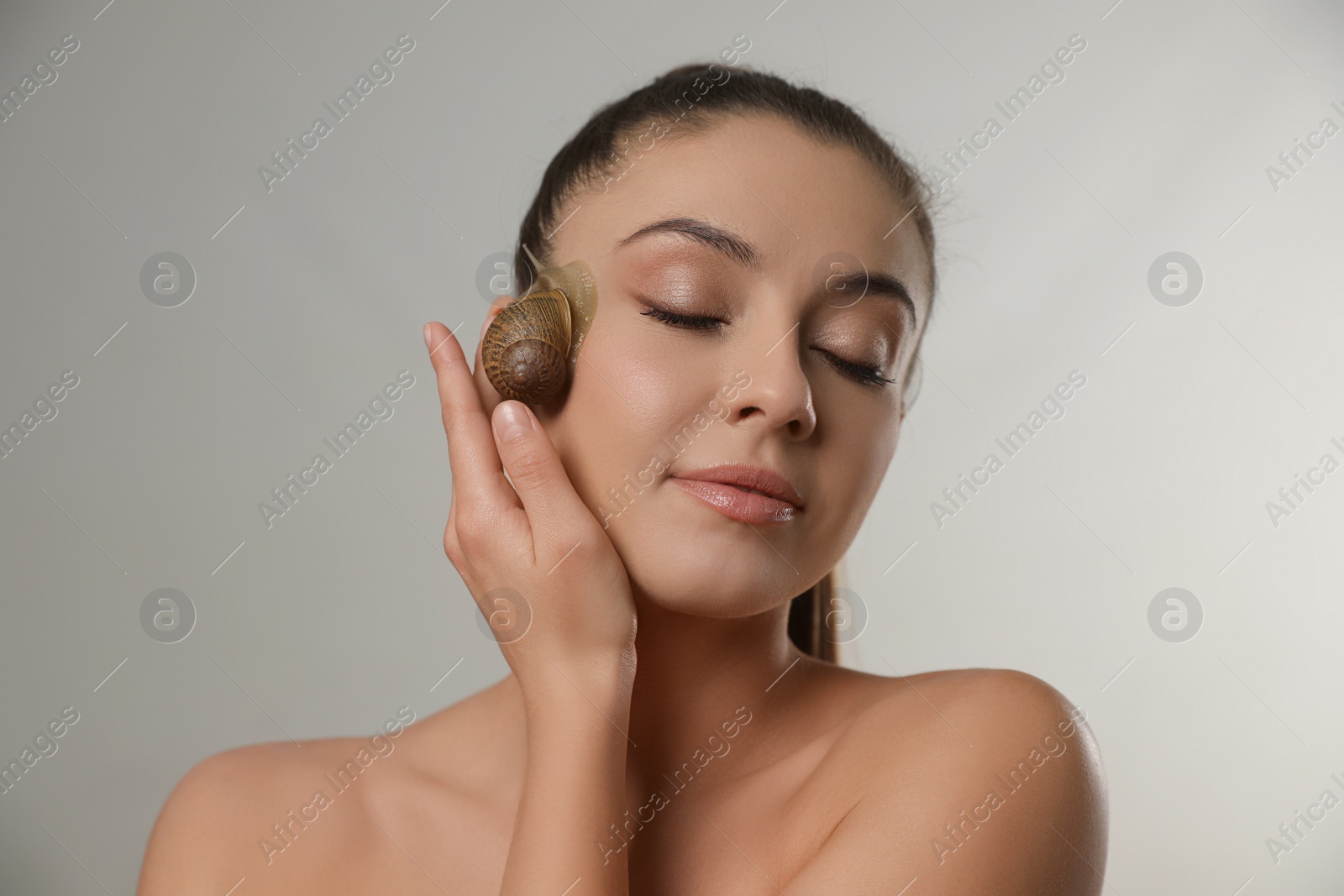 Photo of Beautiful young woman with snail on her face against grey background