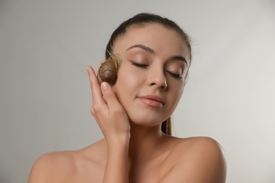 Photo of Beautiful young woman with snail on her face against grey background