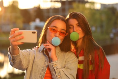 Photo of Beautiful young women blowing bubble gums and taking selfie outdoors