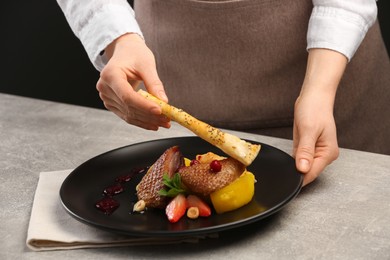 Photo of Food stylist preparing delicious dish with chicken, parsnip and strawberries for photoshoot at grey table in studio, closeup