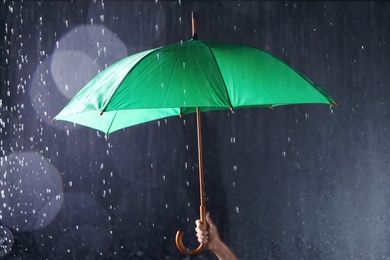 Photo of Woman holding bright umbrella under rain on dark background, closeup