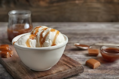 Photo of Tasty ice cream with caramel sauce in bowl on wooden board