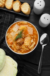 Tasty cabbage soup with meat, carrot and dill served on black wooden table, flat lay
