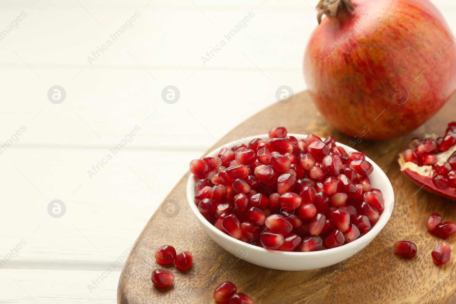 Photo of Ripe juicy pomegranate grains on white wooden table. Space for text