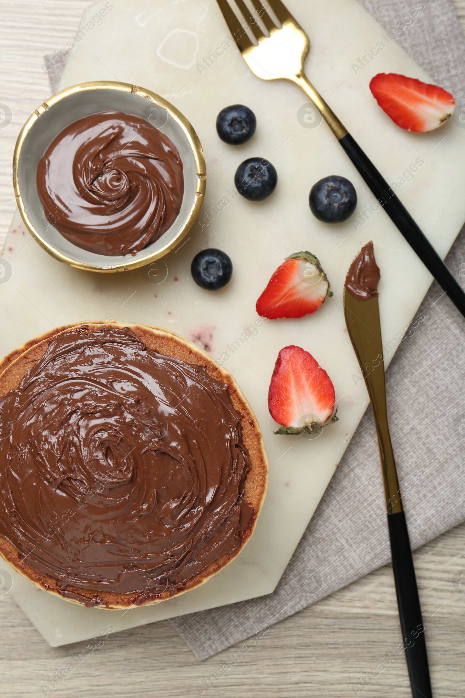 Photo of Delicious pancakes with chocolate paste, berries and cutlery on wooden table, top view