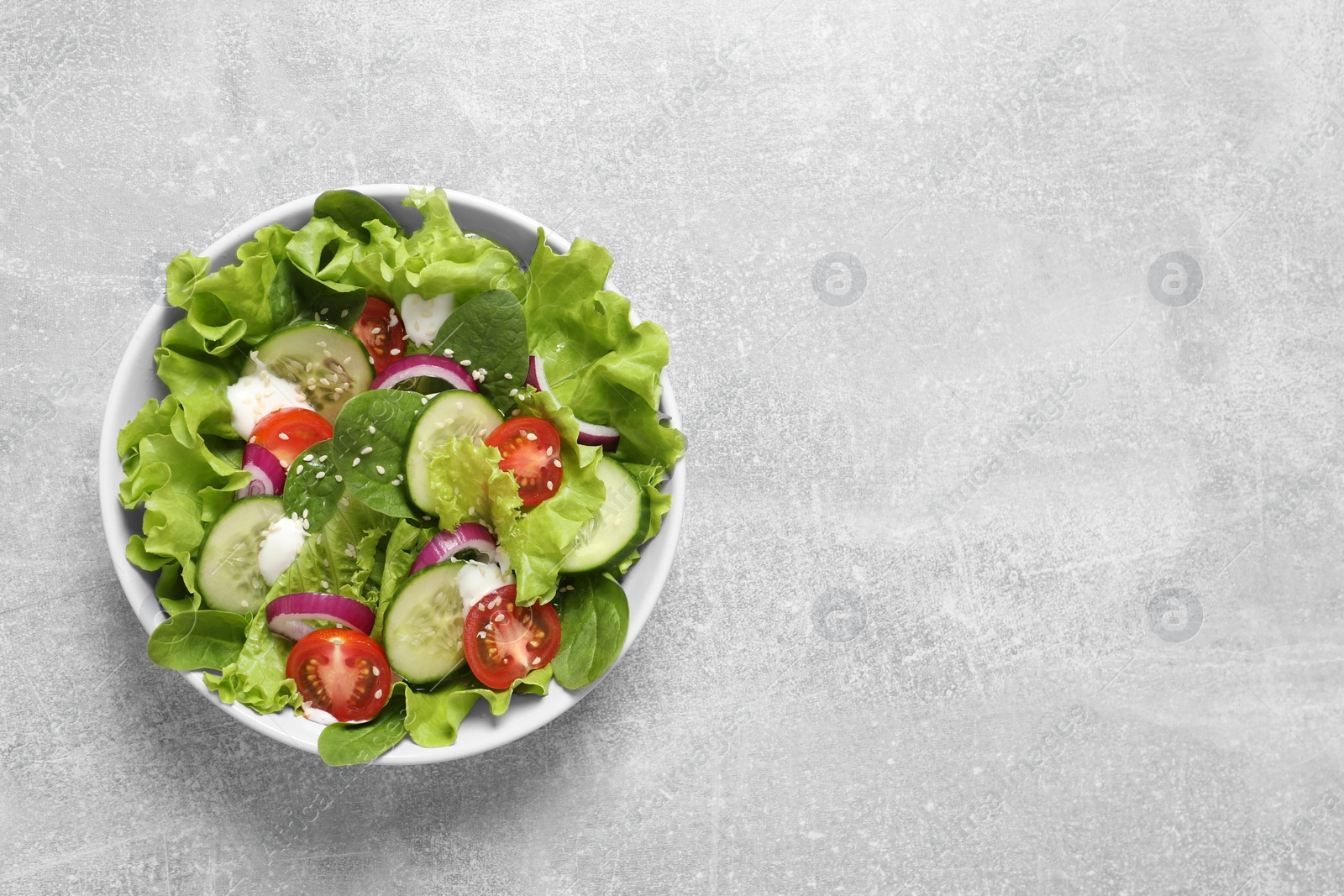 Photo of Delicious salad in bowl on light grey table, top view. Space for text