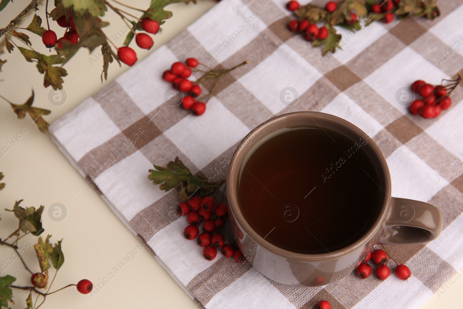 Photo of Brown cup with hawthorn tea and berries on beige table