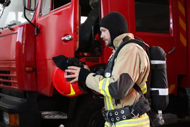 Firefighter in uniform wearing helmet near red fire truck at station