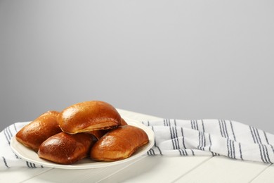 Photo of Delicious baked pirozhki on white wooden table, space for text