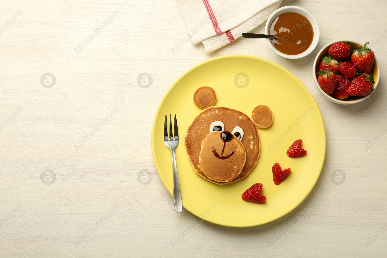 Photo of Creative serving for kids. Plate with strawberries, cute bear made of pancakes on light wooden table, flat lay. Space for text