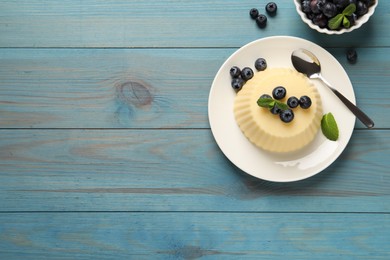 Photo of Delicious semolina pudding with blueberries on light blue wooden table, flat lay. Space for text