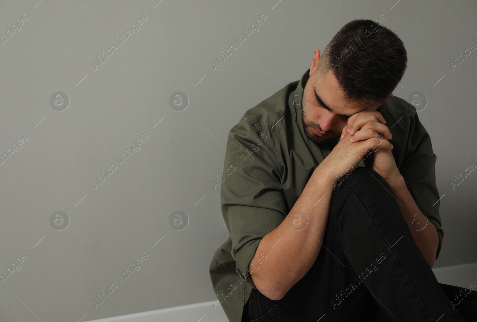 Photo of Sad man sitting near light grey wall. Space for text