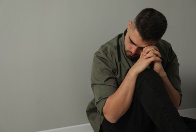 Sad man sitting near light grey wall. Space for text