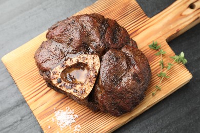 Photo of Piece of delicious grilled beef meat, thyme and salt on black table, top view