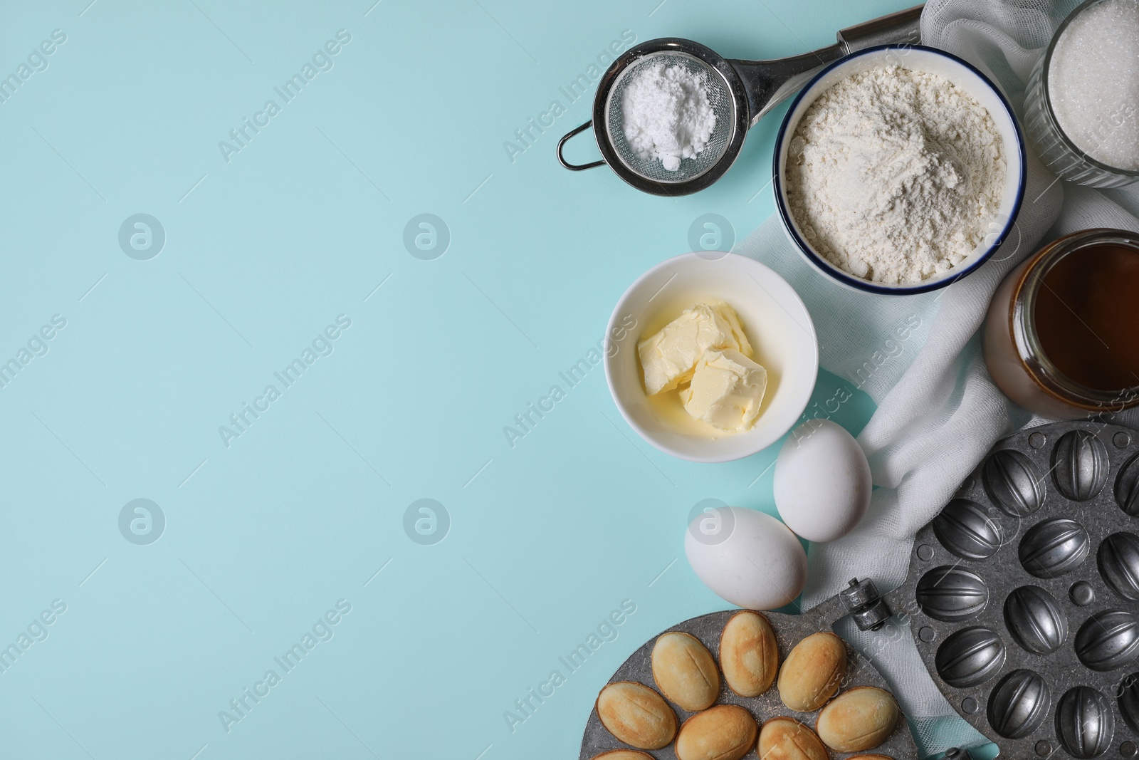 Photo of Freshly baked homemade walnut shaped cookies, baking mold and ingredients on turquoise table, flat lay. Space for text