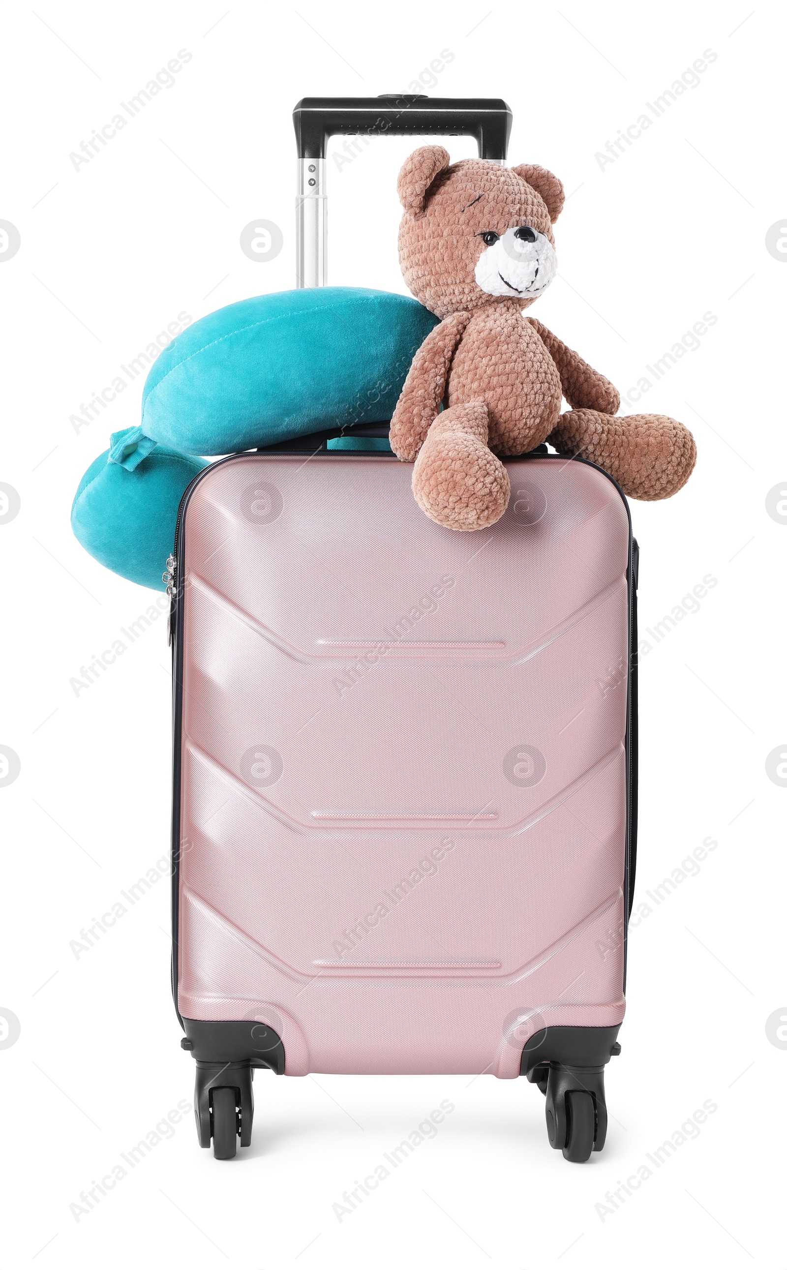 Photo of Light blue travel pillow and toy bear on suitcase against white background