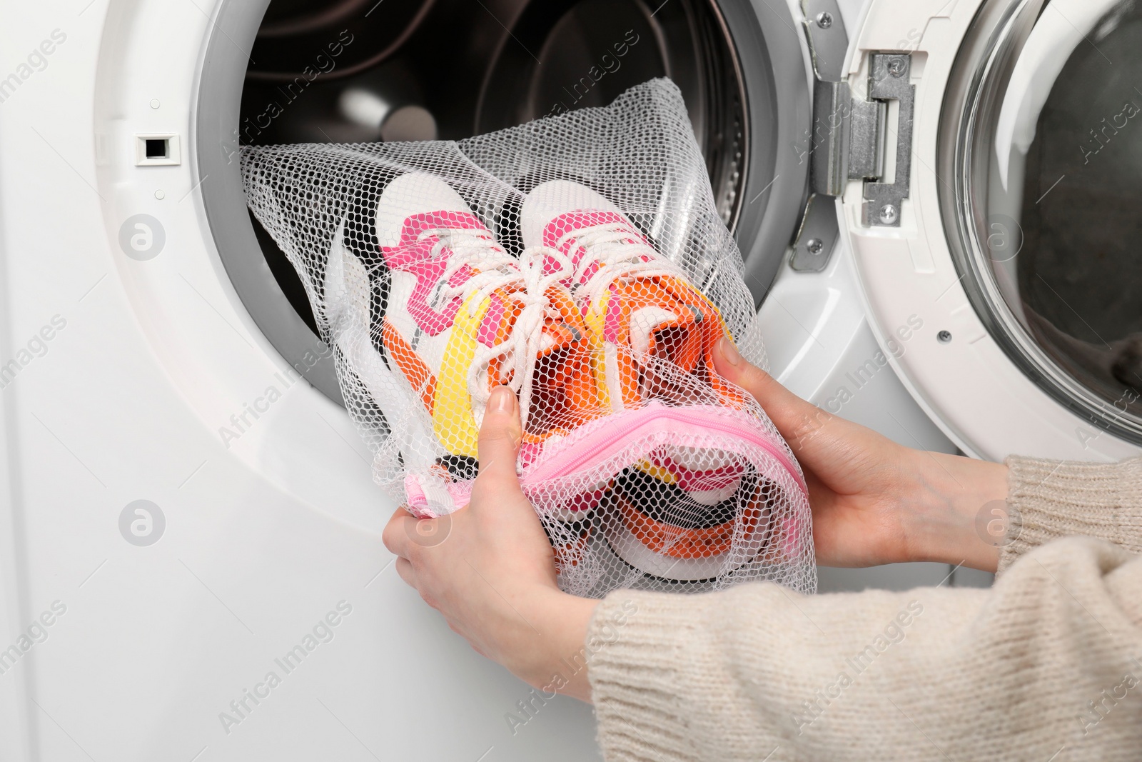 Photo of Woman putting stylish sneakers into washing machine, closeup