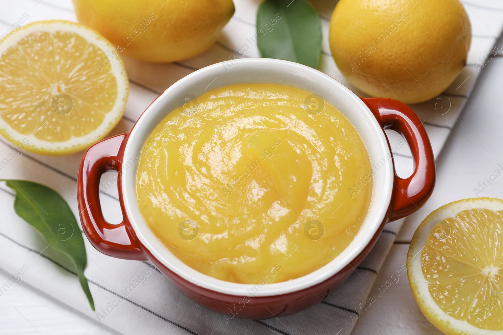 Photo of Delicious lemon curd in bowl and fresh citrus fruits on table, closeup