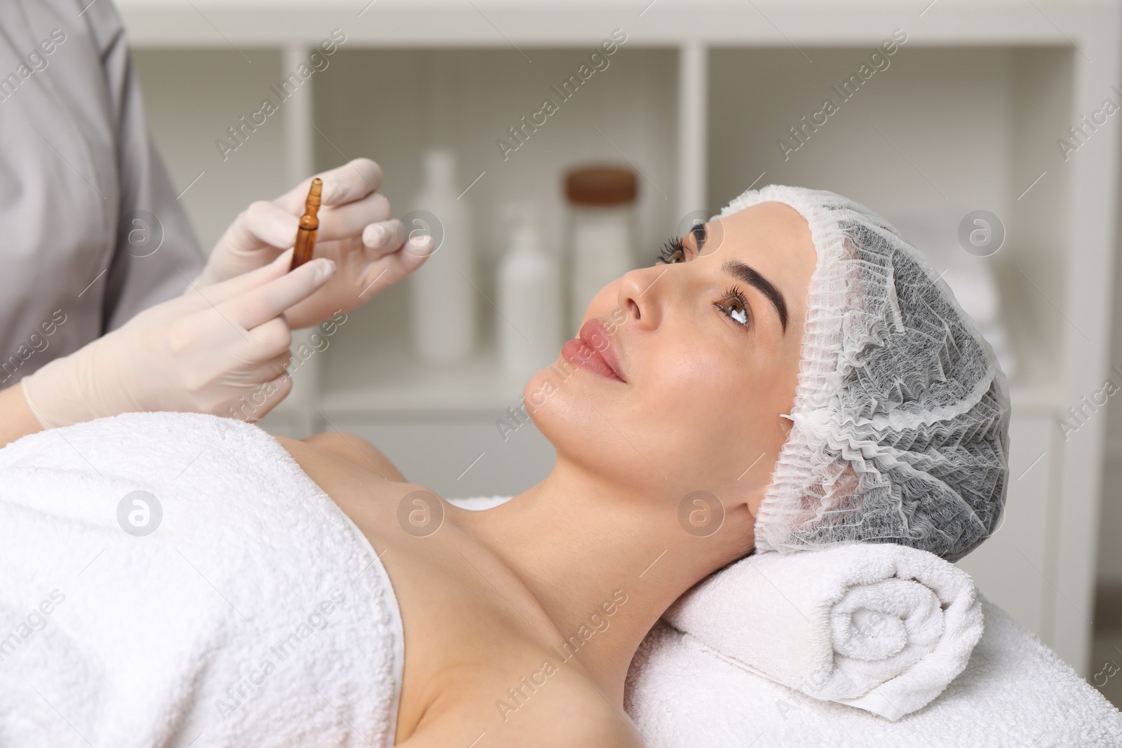 Photo of Professional cosmetologist holding skincare ampoule while working with client in clinic, closeup