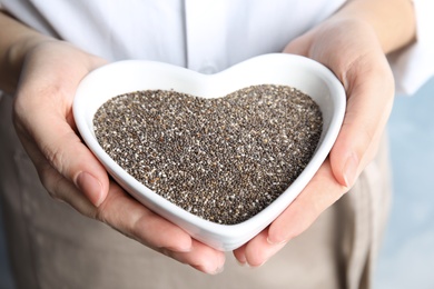 Photo of Woman holding heart shaped bowl with chia seeds on color background, closeup