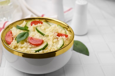 Photo of Tasty couscous with tomatoes, cucumber and basil on white tiled table, closeup. Space for text