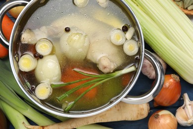 Photo of Pot with tasty bouillon and different ingredients on blue wooden table, flat lay