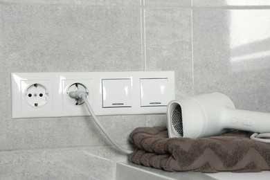 Hairdryer plugged into power socket on light grey wall