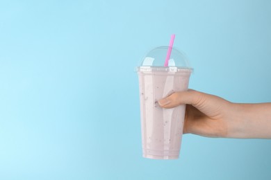 Photo of Woman with plastic cup of tasty smoothie on light blue background, closeup. Space for text