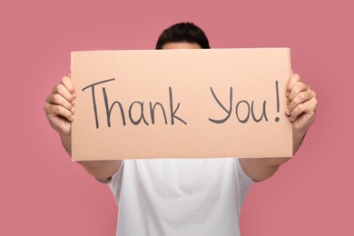 Photo of Man holding cardboard sheet with phrase Thank You on pink background, selective focus