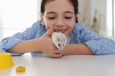 Little girl with cute hamster at table indoors