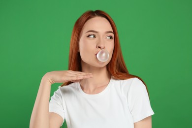 Beautiful woman blowing bubble gum on green background