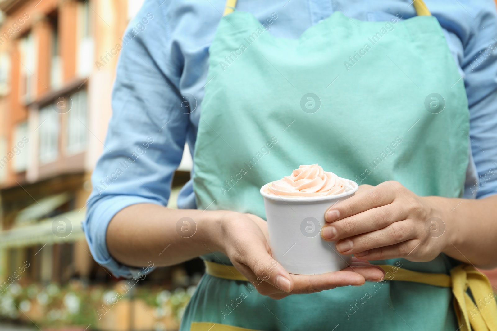 Photo of Woman holding cup with tasty frozen yogurt outdoors, closeup