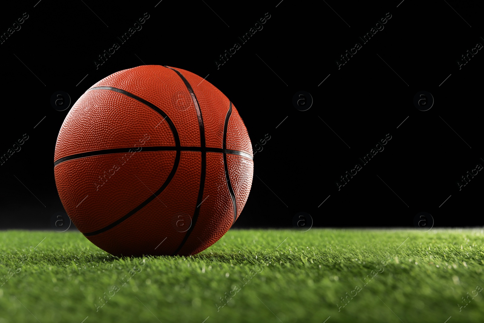 Photo of Basketball ball on green grass against black background, space for text