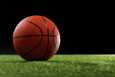 Basketball ball on green grass against black background, space for text
