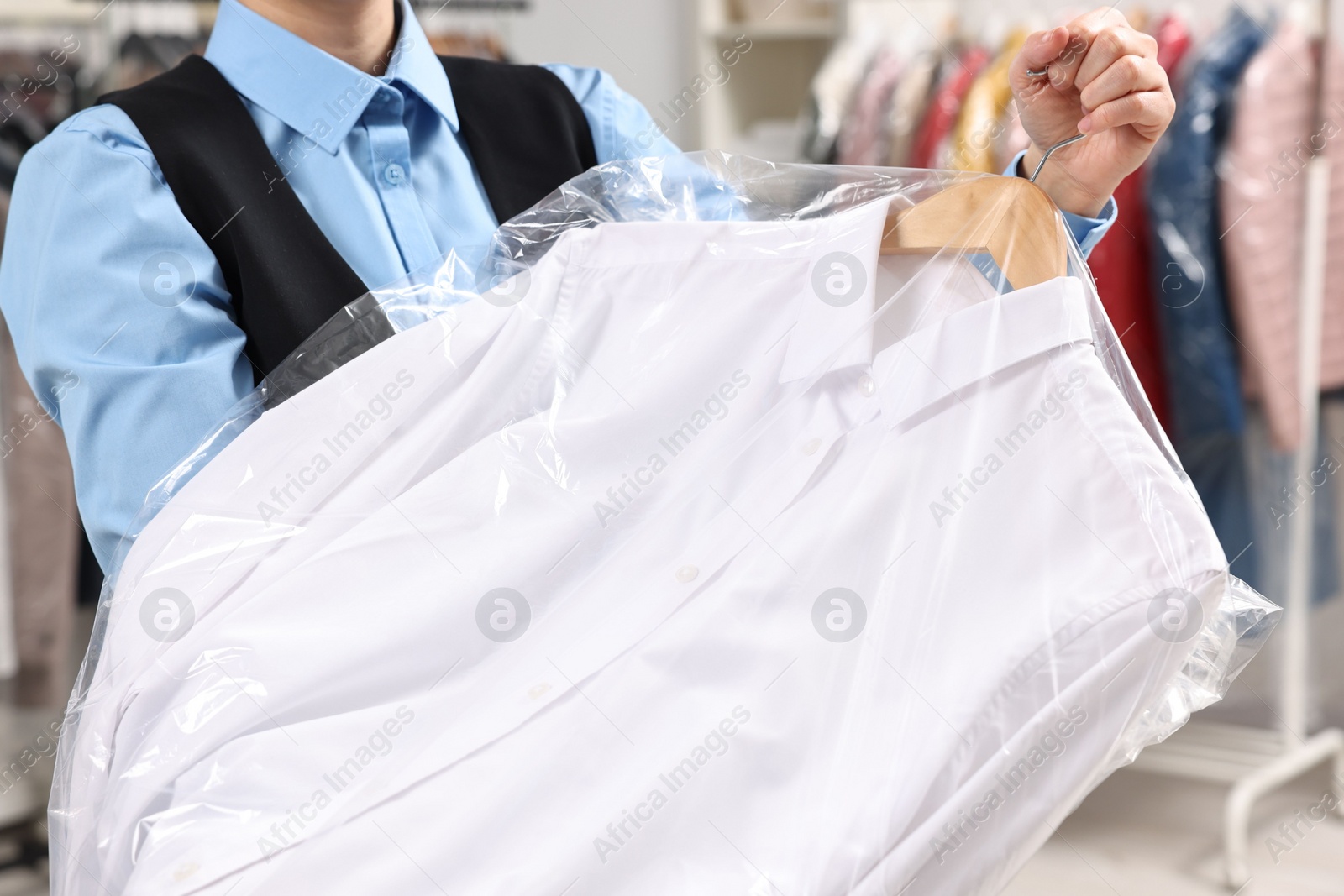 Photo of Dry-cleaning service. Woman holding shirt in plastic bag indoors, closeup