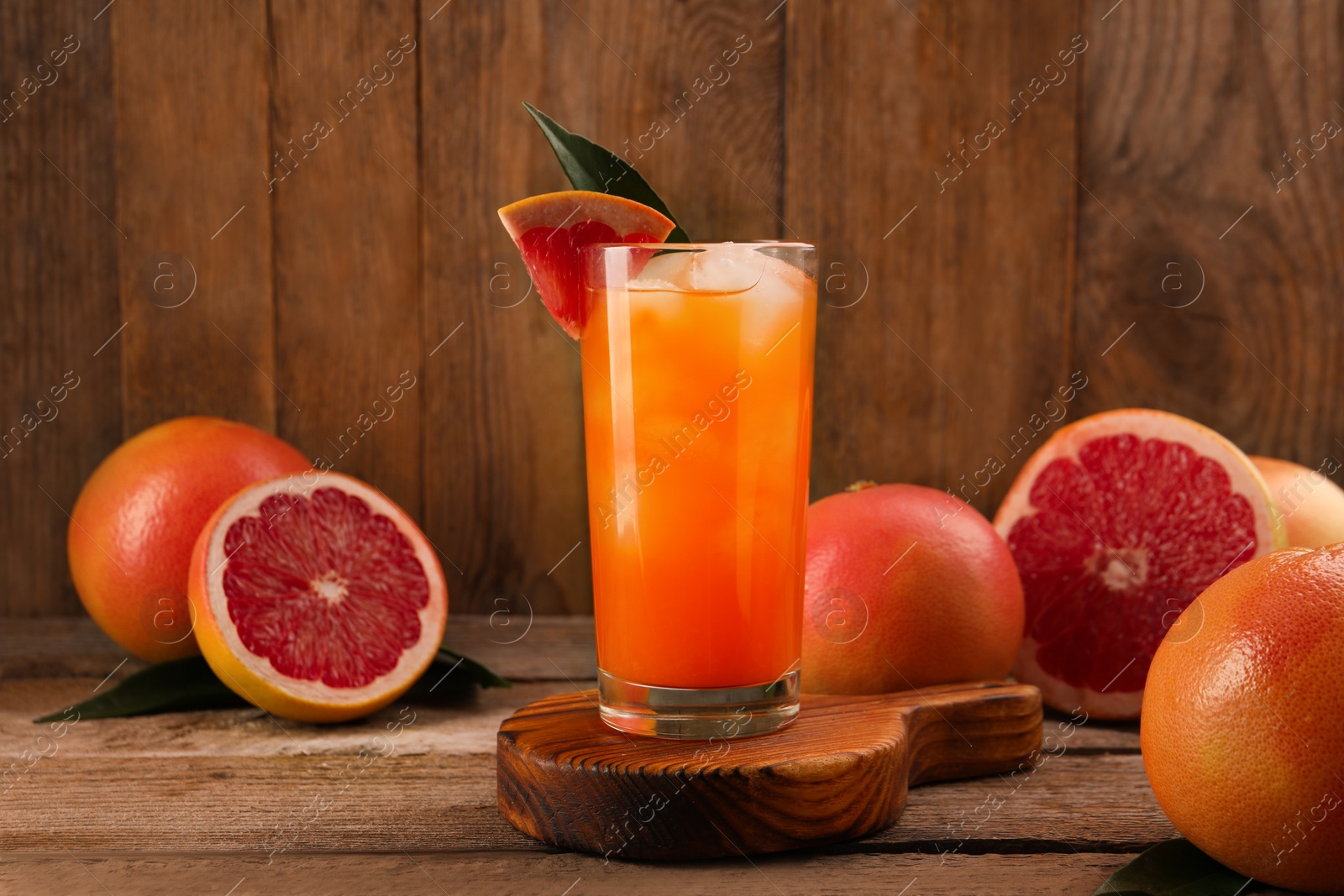 Photo of Tasty grapefruit drink with ice in glass and fresh fruits on wooden table