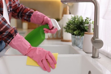 Woman with spray bottle and microfiber cloth cleaning sink in kitchen, closeup