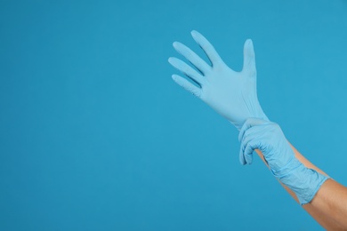 Doctor wearing medical gloves on light blue background, closeup. Space for text