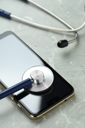 Modern smartphone and stethoscope on grey table