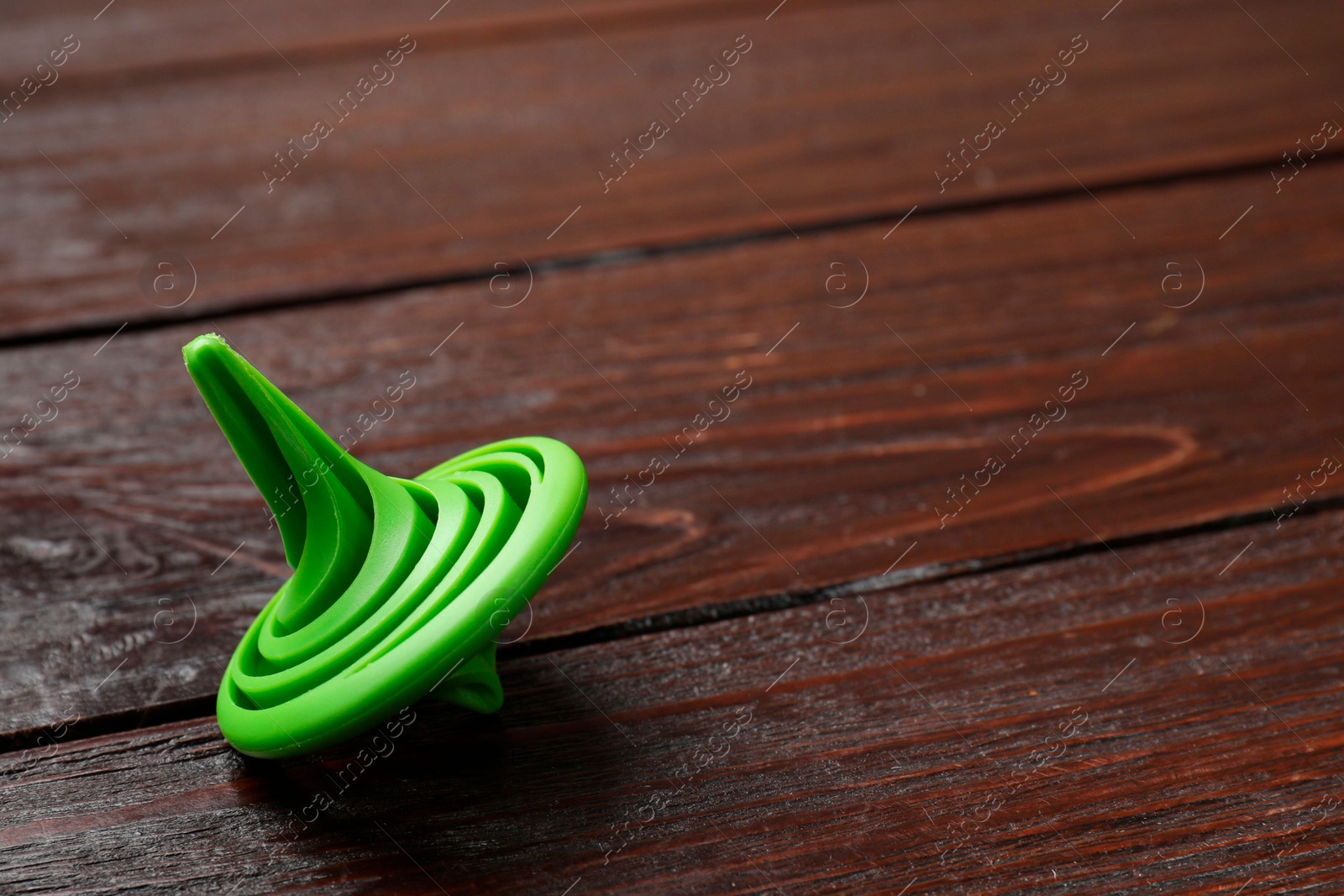 Photo of One green spinning top on wooden table, closeup. Space for text