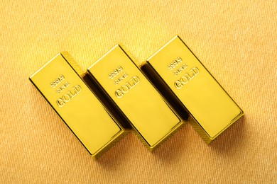 Photo of Many shiny gold bars on yellow fabric, flat lay
