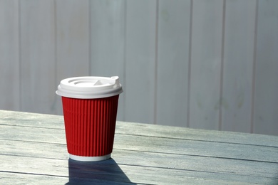Cardboard coffee cup with lid on wooden table. Space for text