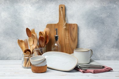 Photo of Different kitchenware and dishware on white wooden table against textured wall