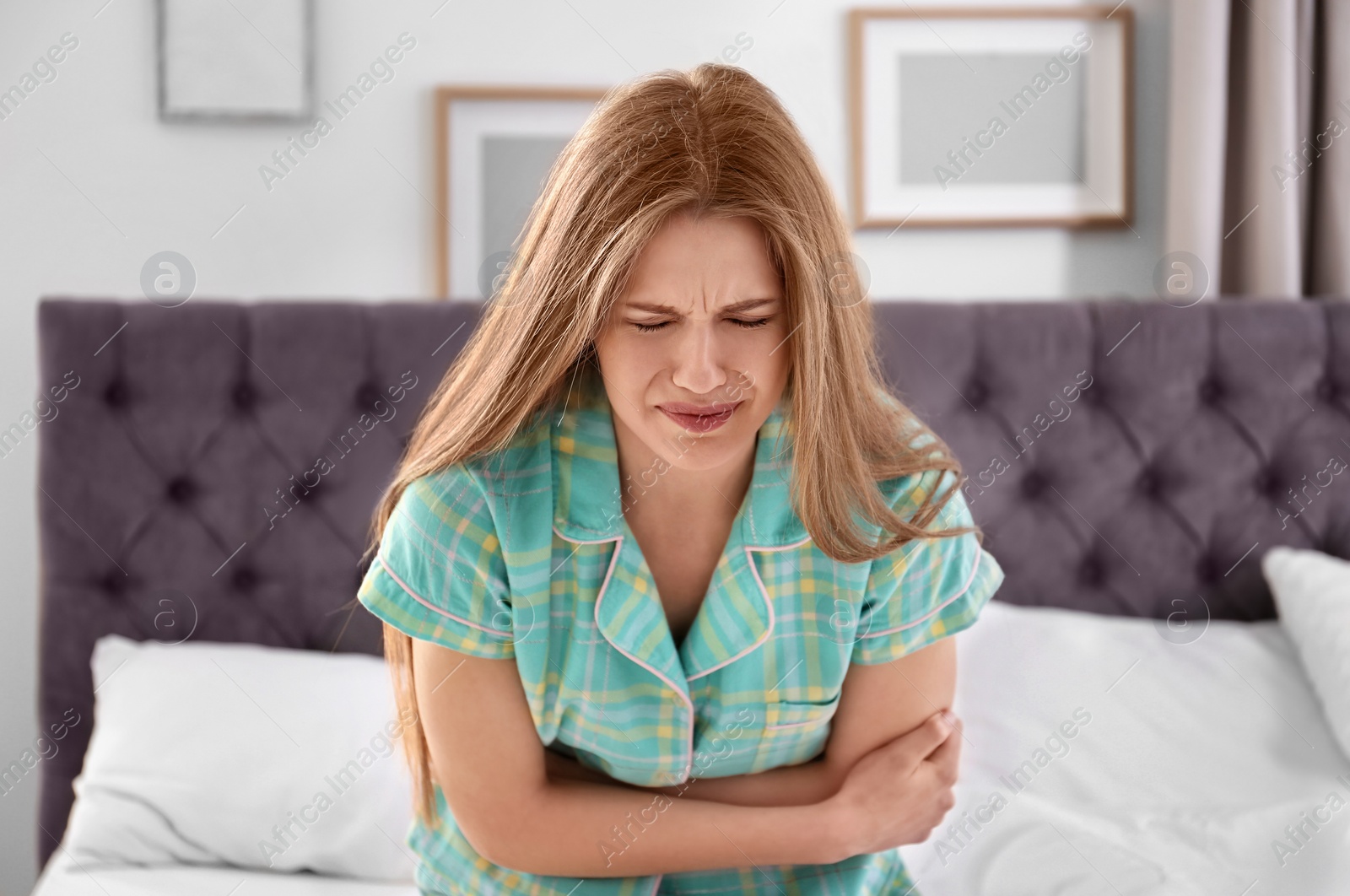 Photo of Young woman suffering from stomach ache in bedroom