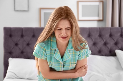 Photo of Young woman suffering from stomach ache in bedroom