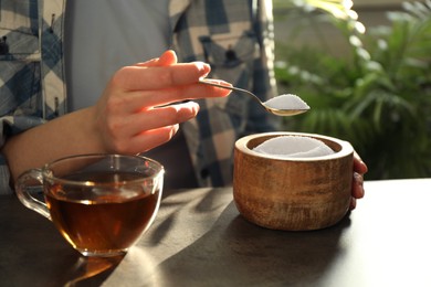 Woman adding sugar into cup of tea at dark table, closeup