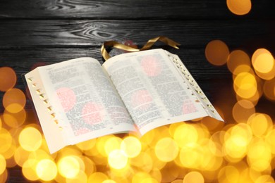 Open Bible on black wooden table, bokeh effect