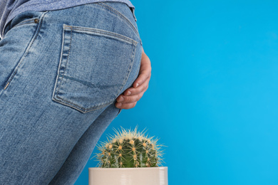 Photo of Man sitting down on cactus against light blue background, space for text. Hemorrhoid concept