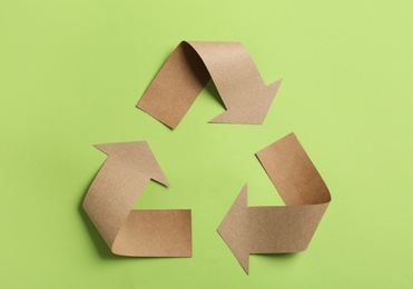 Photo of Recycling symbol cut out of kraft paper on green background, top view