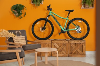Image of Modern bicycle near orange wall and comfortable armchairs in stylish living room interior